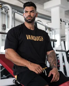 Close-up van een zwart oversized katoenen fitness t-shirt met een goudkleurig Vanquish logo.
