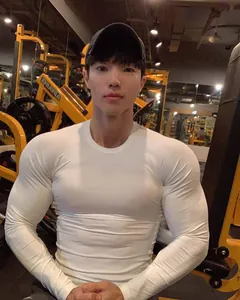 Detailansicht eines weißen Langarm-Kompressionsshirts an einem muskulösen Modell im Fitnessstudio.