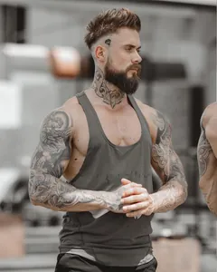 Muscular male model wearing a grey breathable elastic fitness tank top in a professional gym setting