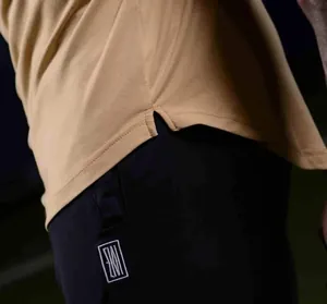 Close-up detail of tan fitness T-shirt hem and black shorts with embroidered logo