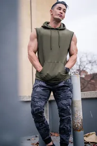 Men's sleeveless olive green fitness gym hoodie vest worn by a muscular model outdoors.
