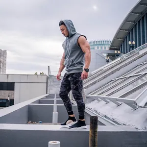 Fitness model wearing a grey sleeveless gym hoodie and camo joggers on a rooftop