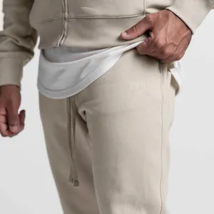 Detailansicht einer beigen Herren-Jogginghose mit Kordelzug und dezentem Prägelogo.