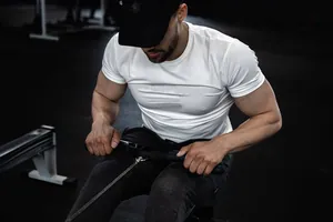 Close-up of a muscular man in a white fitness t-shirt using a rowing machine in a gym