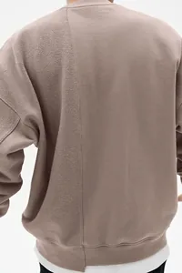 Detalle de sudadera cuello redondo malva con textura de tela empalmada y hombros caídos