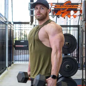 Hombre musculoso con camiseta de tirantes de algodón verde oliva con mancuernas en el gimnasio