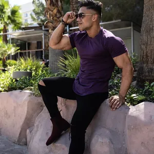 Muscular athletic man wearing a purple fitted t-shirt in an outdoor palm tree setting.