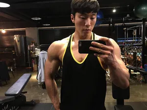 Gespierde man in een zwart fitness hemdje met gele rand in een professionele sportschool.
