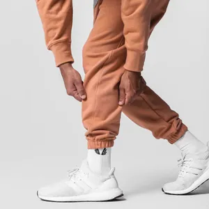 Detail view of terracotta cotton sweatpants with elastic cuffs and white sneakers.