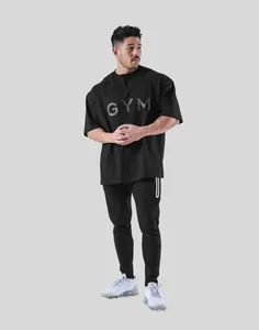 Full body view of a man wearing a black oversized gym t-shirt with black joggers