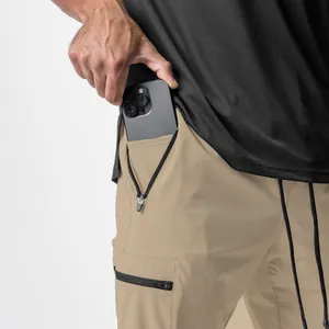 Detailansicht khakifarbene Cargohose mit tiefer Reißverschlusstasche und Smartphone