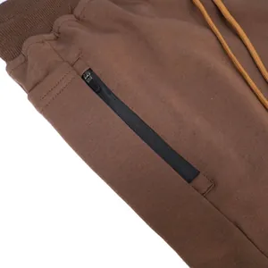 Close-up of brown cotton sports shorts featuring a black zipper pocket and drawstring waist.