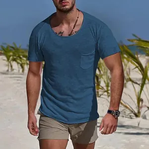 Vue détaillée d'un t-shirt bleu pour hommes à col rond et poche dans un décor de plage.