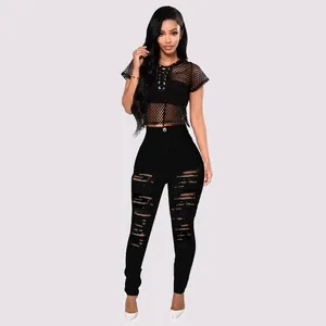 Full view of model wearing black high waist ripped skinny jeans and a mesh crop top.
