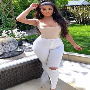 Dettaglio di jeans skinny bianchi strappati a vita alta su una modella in un giardino.