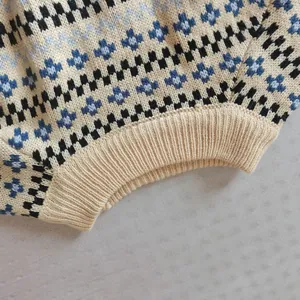 Primo piano dettagliato di un maglione beige in maglia con motivi a croce geometrici blu.