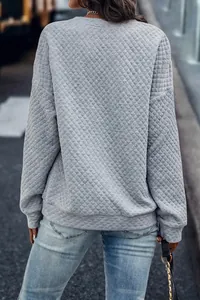 Vista trasera de una sudadera gris acolchada de manga larga con textura de rombos y hombros caídos