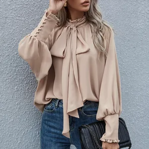Detail einer eleganten beigen Stehkragenbluse mit Schleife und schicken Puffärmeln.
