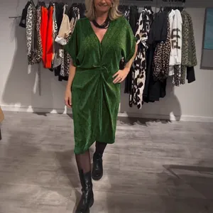 Grünes Midi-Kleid mit V-Ausschnitt und Metallic-Effekt für Damen im Showroom.