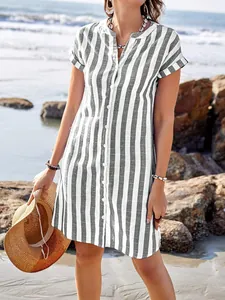 Detailed view of a woman wearing a casual striped shirt dress on a sunny beach background.
