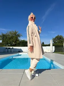 Scatto lifestyle di un cappotto teddy crema con strisce nere accanto a una piscina blu.