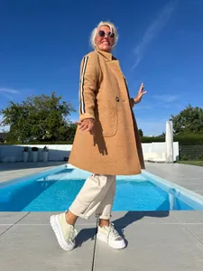 Donna elegante in cappotto di lana d'agnello cammello con strisce vicino a una piscina.