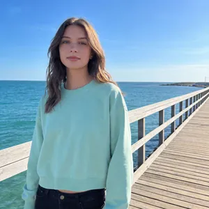 Woman in light green cropped cotton sweatshirt standing on a scenic pier by the sea
