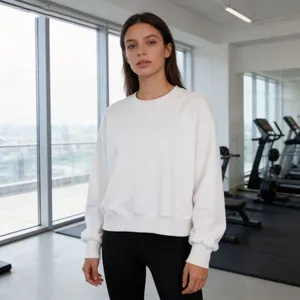 Full body view of a woman wearing a white cropped crewneck sweatshirt in a gym setting.