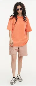 Full body view of a female model wearing an orange acid-washed oversized heavy cotton t-shirt.