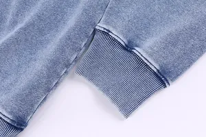 Detail view of acid-washed denim hoodie showing ribbed cuff and distressed texture