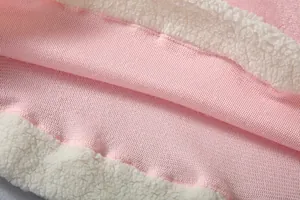 Macro detail of soft pink fleece and white sherpa lining on warm wearable blanket.