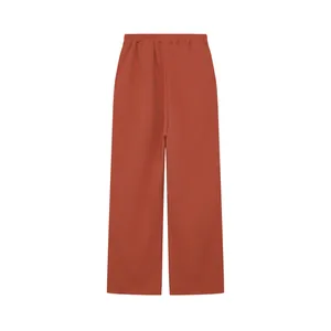 Dettaglio pantaloni a gamba larga che mostra la vestibilità ampia e il tessuto rosso mattone