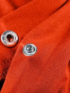 Dettaglio ravvicinato di bottone automatico in metallo argento su giacca arancione