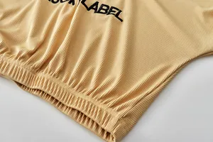 Detailansicht von Rippenstoff mit schwarzer LUCKY LABEL Stickerei auf einem beigen Anzug