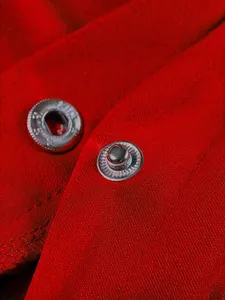 Dettaglio dei bottoni a pressione argentati sul tessuto rosso vivo della giacca varsity