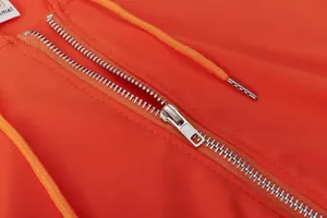 Detailed view of the silver metal zipper on a vibrant orange sporty sweatshirt.