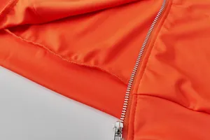 Detailed close-up of silver metal zipper and stitching on orange tracksuit jacket