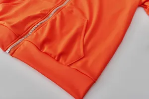 Macro detail showing orange tracksuit zipper pocket texture and ribbed hem stitching