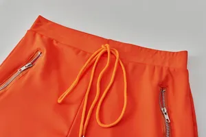 Close-up of bright orange sports pants featuring adjustable drawstring and silver zipper pockets
