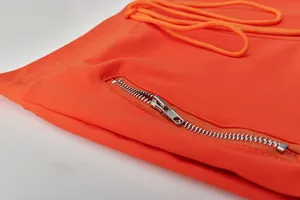 Detailed view of the metallic zipper pocket and fabric on a bright orange tracksuit