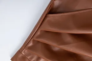 Close-up detail showing the pleated texture and fine stitching of the brown PU leather skirt.