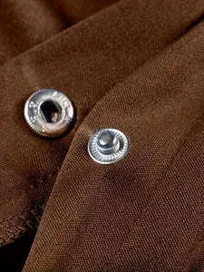 Dettaglio macro di bottoni a pressione in metallo su tessuto strutturato marrone di una giacca