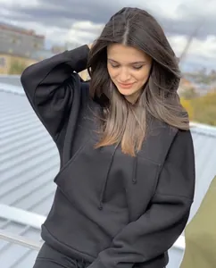 Κοντινή λήψη κομψού μαύρου oversized φούτερ με κουκούλα, μπροστινή τσέπη και κορδόνια.