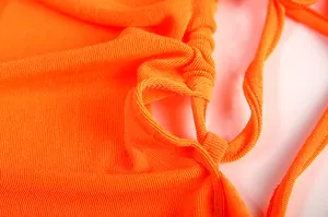 Close-up view of vibrant orange ribbed knit fabric and tie-up detail of a backless dress.