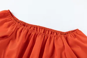 Détail en gros plan de l'encolure élastique à volants de ce haut orange vif au tissu fluide