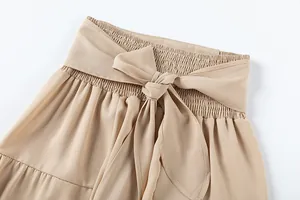 Gros plan d'un pantalon beige taille haute avec détail nœud papillon à la taille.