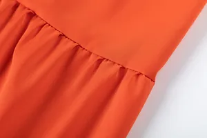 Gros plan des coutures fines et du plissé sur ce pantalon large orange éclatant.