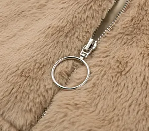Close-up detail of a circular silver metal zipper pull on a soft camel faux fur plush jacket.