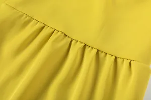 Détail macro de la couture froncée et de la texture fluide sur un pantalon jaune