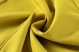 Gros plan sur la texture du tissu jaune montrant un drapé souple et un tissage fin